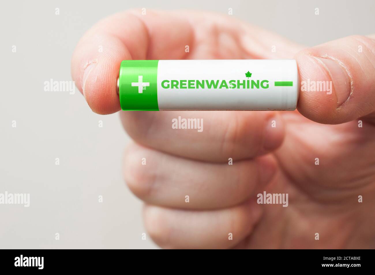 Mann hält eine grün-weiße Batterie mit dem Wort Greenwashing aufgedruckt. Greenwashing ist eine Kommunikationstechnik, die darauf abzielt, ein falsches Bild zu erstellen Stockfoto