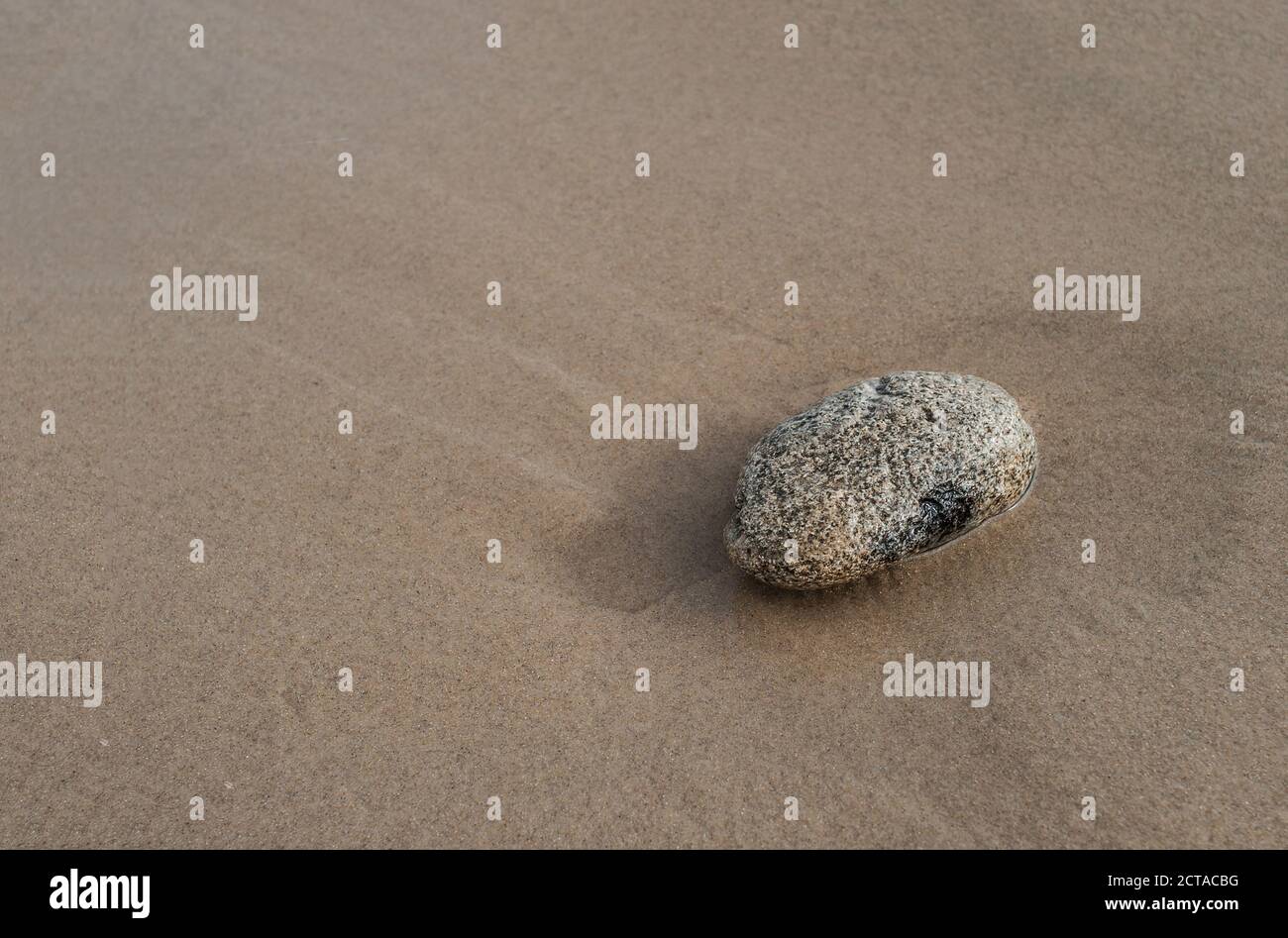 Stein liegt an einem Sandstrand. Sommer entspannenden Hintergrund mit Kopierplatz. Konzept - einsam, aber stark. Stockfoto