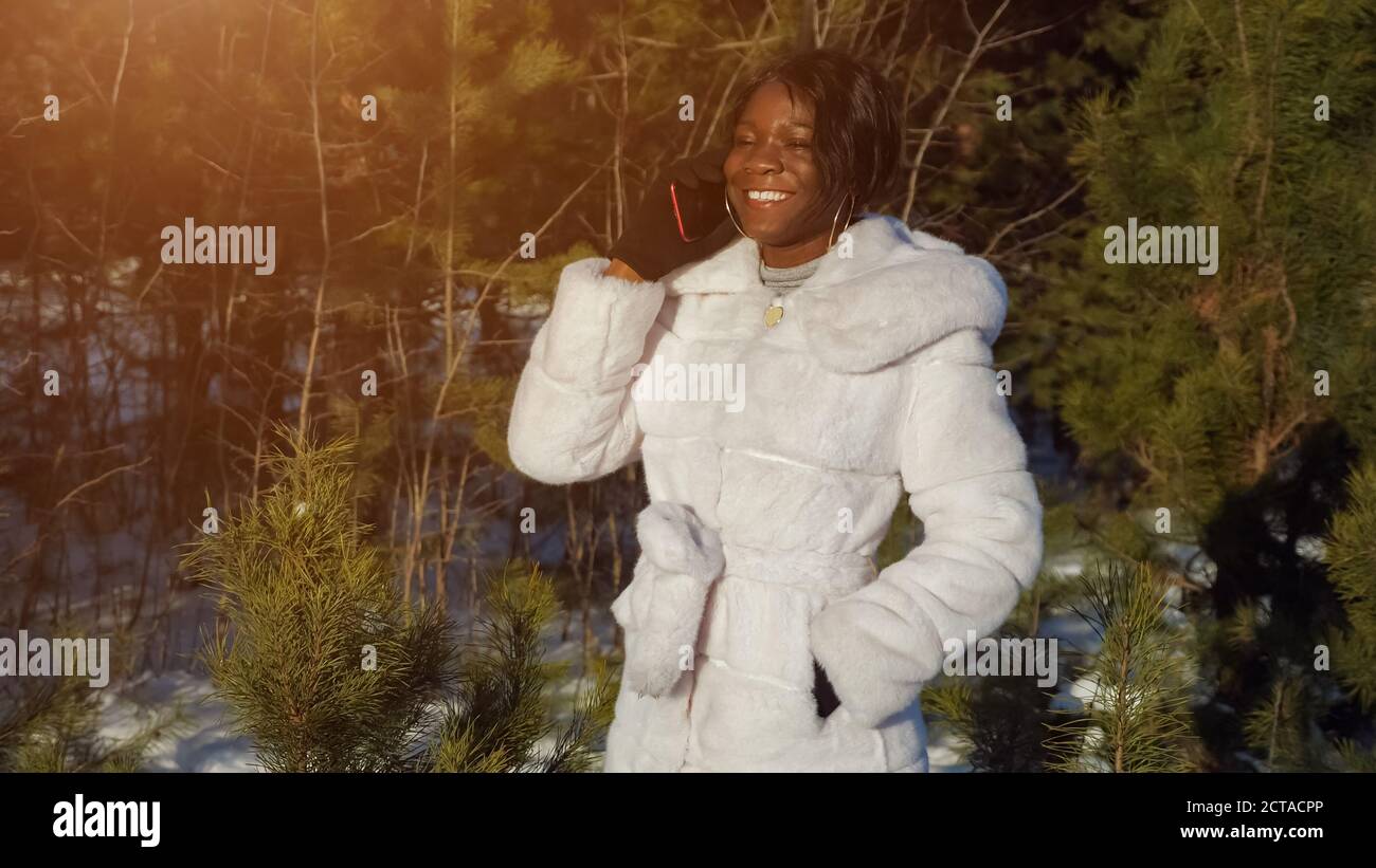 Schwarze Frau in Ohrringen spricht über digitale Gadget mit Freunden Stehen gegen immergrüne Kiefern im Wald Nahaufnahme Stockfoto