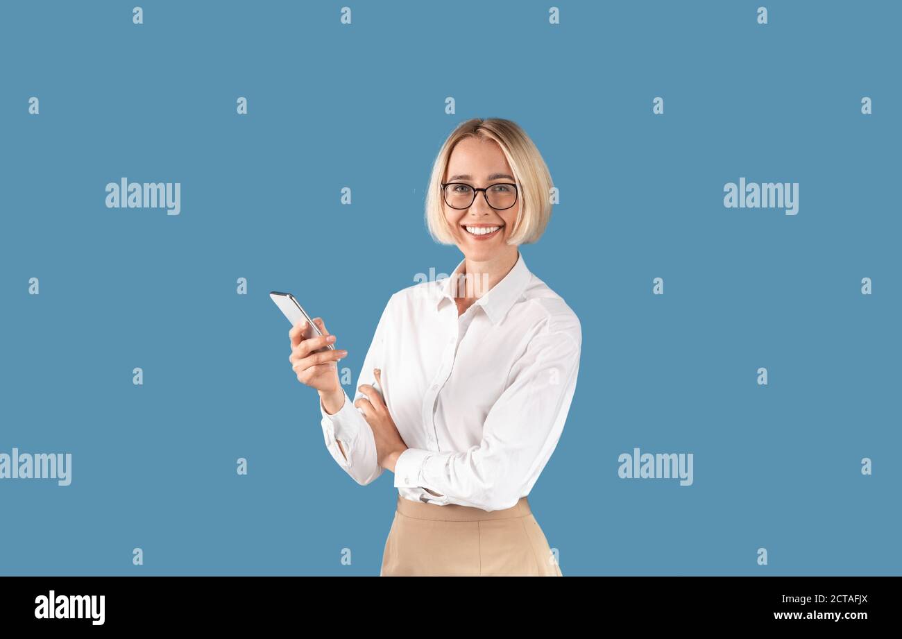 Selbstbewusste Geschäftsfrau mit Smartphone lächelnd und Blick auf die Kamera Vor blauem Studiohintergrund Stockfoto