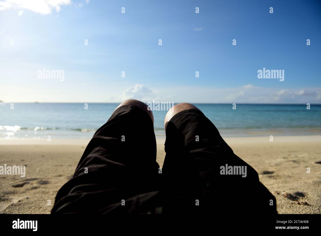 Standpunkt des Mannes, der sich am einsamen karibischen Inselstrand mit blauem Wassermeer, verschwommener Hintergrund entspannt Stockfoto