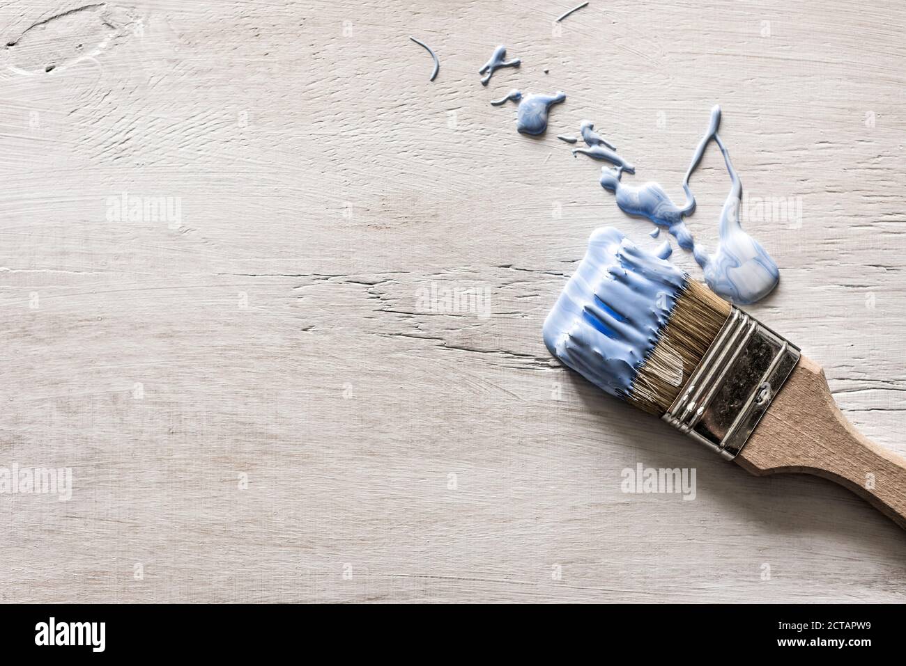 Ein blauer Pinsel liegt auf einem grauen Holzhintergrund Alt und Lackspritzer verschüttet Stockfoto