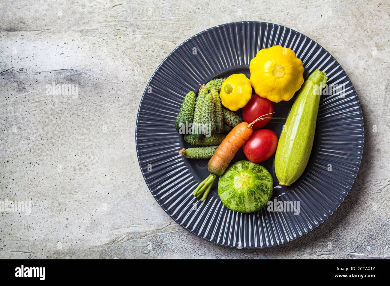 Mini Gemüse Konzept. Mini Zucchini, Tomaten, Gurken, Kürbis und Karotten auf einem dunklen Teller. Stockfoto