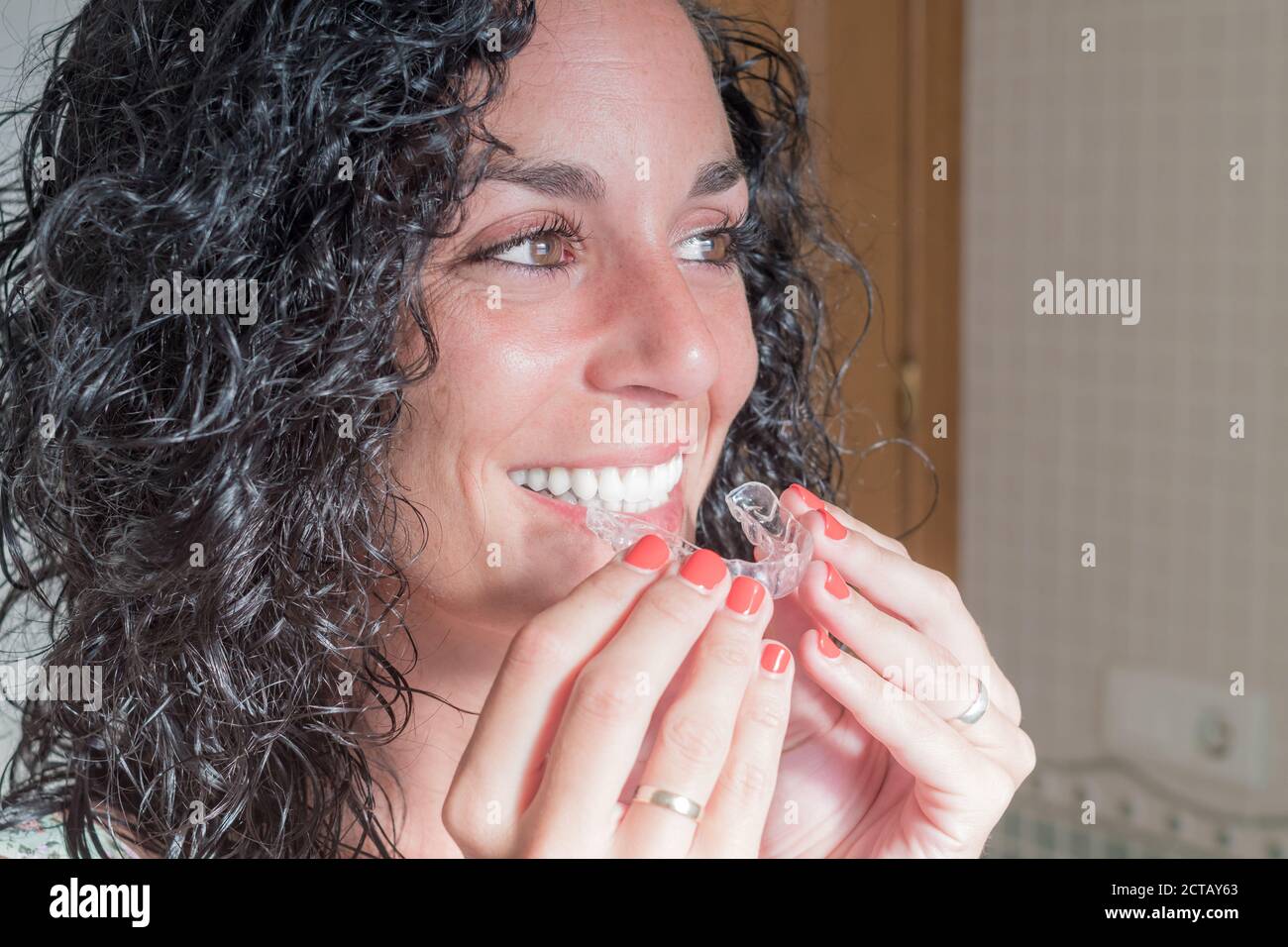 Nahaufnahme von jungen lockigen Haaren Brünette Frau setzen auf ihre unsichtbare Silikon Aligner. Zahnkorrektur. Mobile Kieferorthopädie Stockfoto