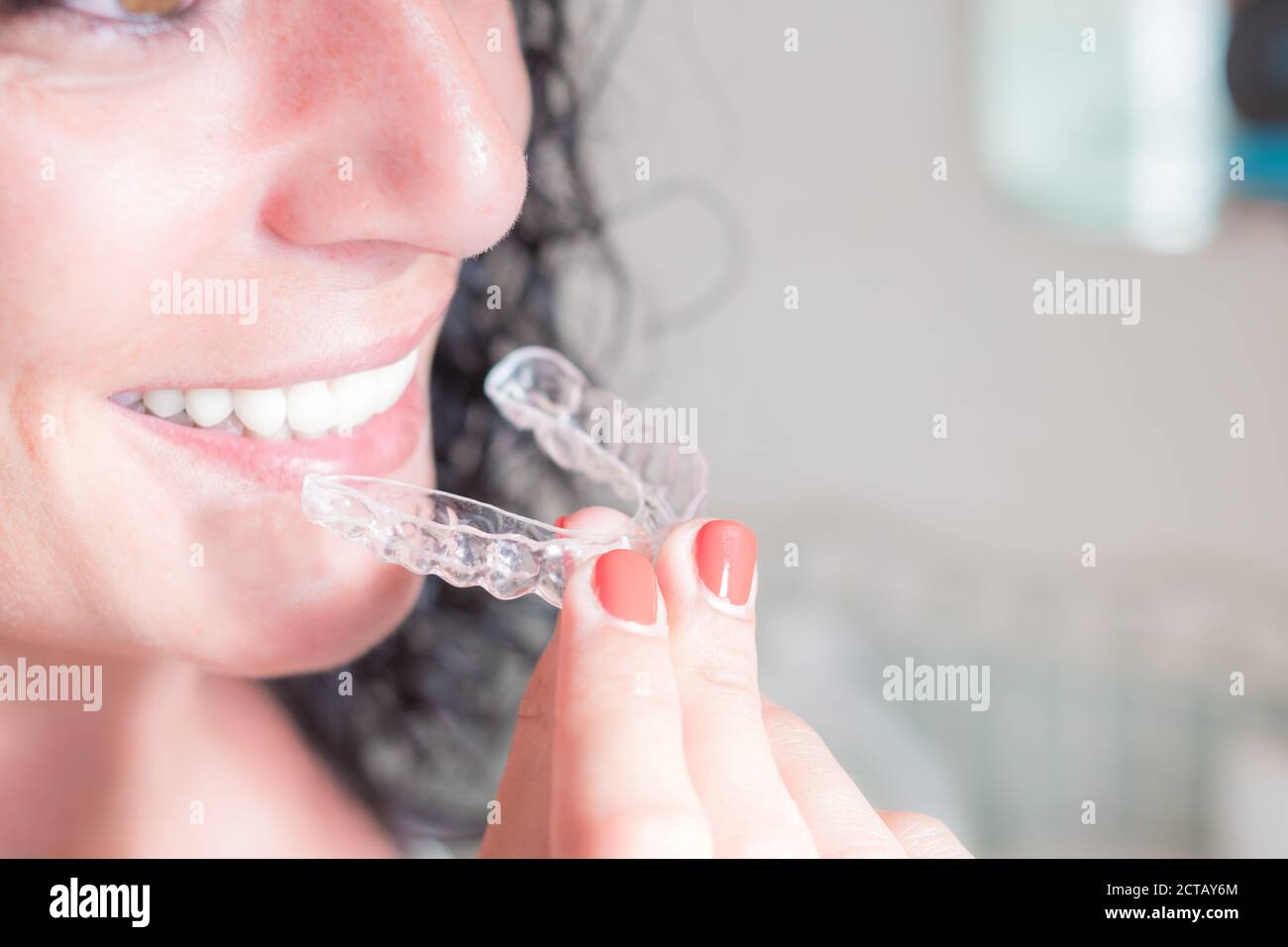 Nahaufnahme des Gesichts und der Hand einer jungen lockigen Brünette Frau lächelnd setzen auf ihre unsichtbare Silikon-Aligner für die Zahnkorrektur. Dental tr Stockfoto