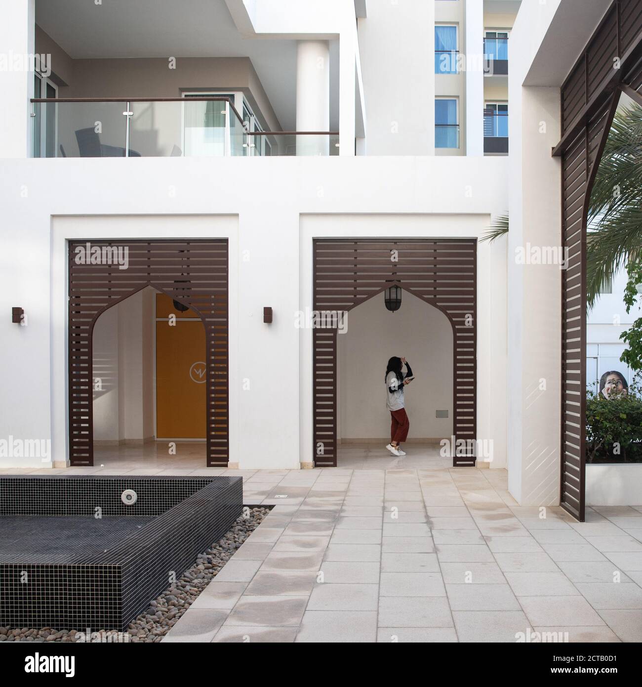 Frau, die in einem Wohngebäude mit Wasserspiel zu Fuß unterwegs ist. Apartments mit Balkon. Al Mouj, die Welle, Maskat, Sultanat von Oman. Februar 13, 2020 Stockfoto