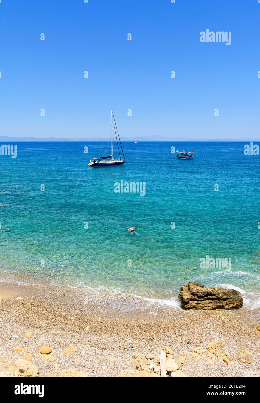 Ein Mann schwimmt am Kiesstrand neben Rhodos-Stadt, Rhodos-Insel, Dodekanes, Griechenland Stockfoto