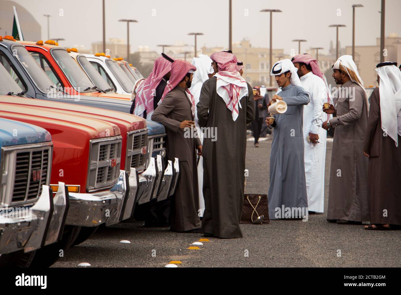 Eine Gruppe kuwaitischer Männer, die in dishdashas gekleidet sind, genießt eine Tasse arabischen Kaffee gewürzt mit Kardamom, wenn sie ihre alten GMC-Lastwagen ausstellt. Stockfoto