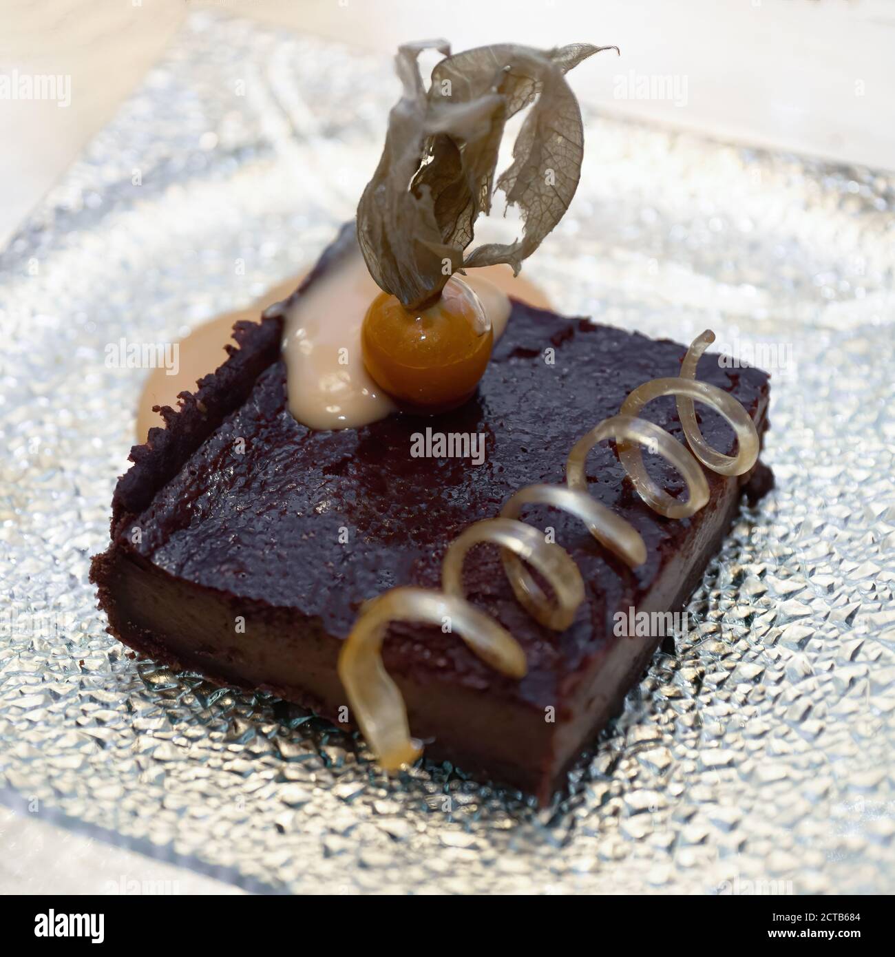 Ein Stück Schokoladenkuchen mit einem karamellisierten peru-Hahn. Zuckerspirale in einer Glasplatte. Stockfoto