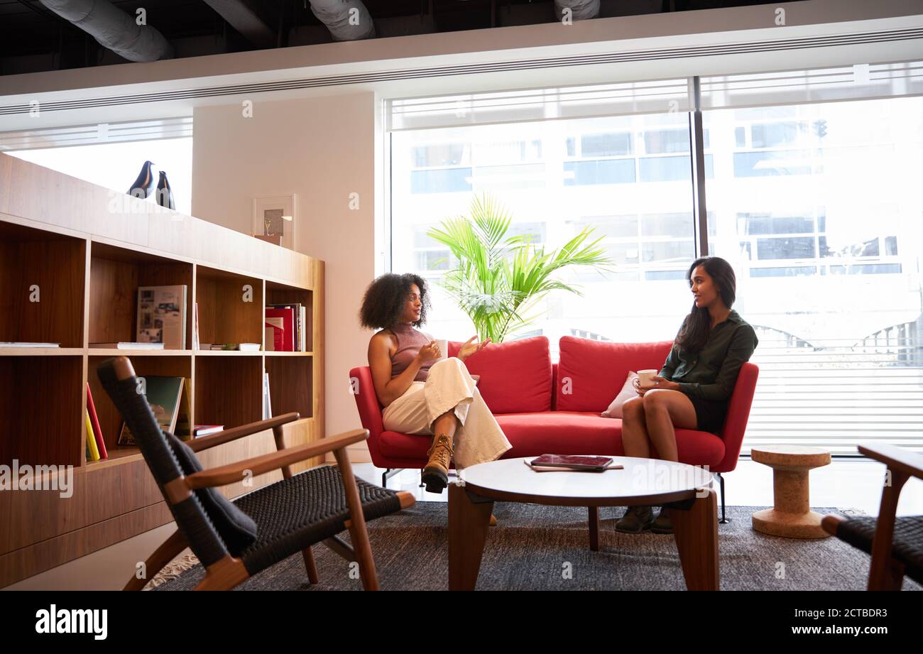 Zwei Geschäftsfrauen Mit Gesellschaftlich Distanzierten Meeting Sitzen Auf Office Sofa Während Der Gesundheitsinpandemie Stockfoto