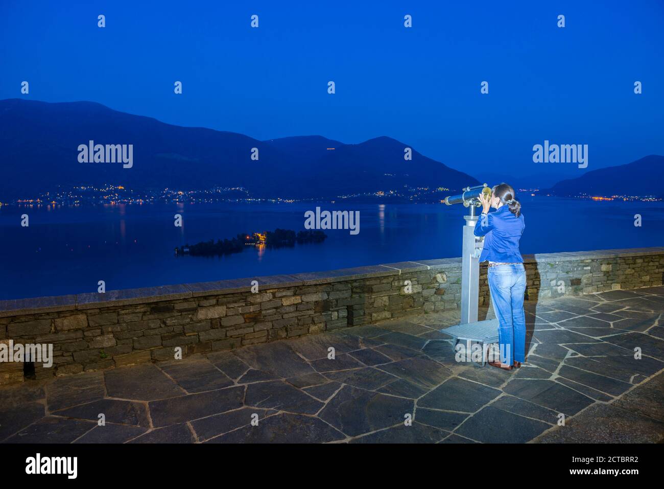 Frau mit Teleskop in Blue Hour und Brissago iIlands am Alpinen Lago Maggiore mit Berg im Tessin, Schweiz. Stockfoto