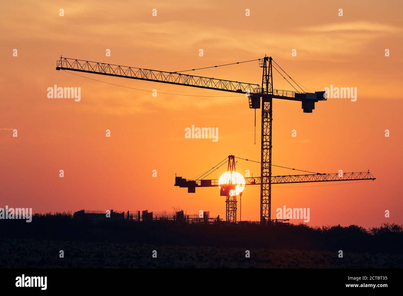 Bauaktivitäten auf Baustellen. Silhouetten von Kränen gegen die Sonne. Stockfoto