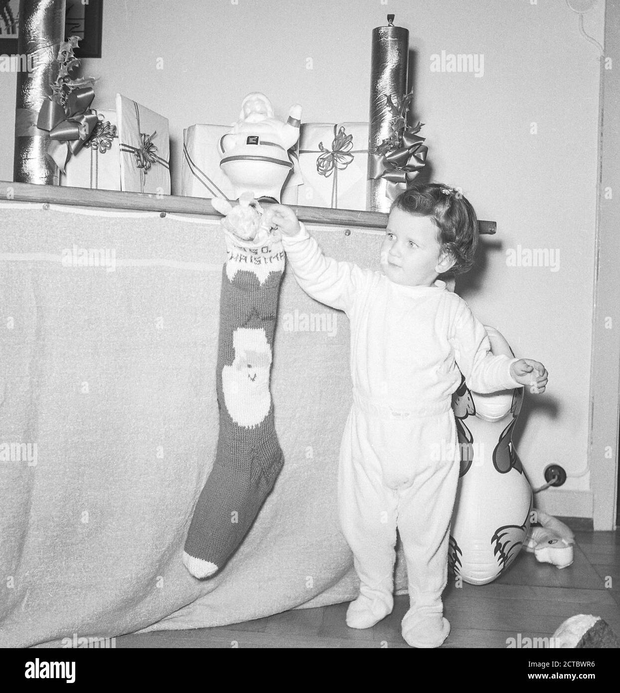 Zwei Jahre altes Mädchen, das ihren Weihnachtsstrumpf hängend, 1951, USA Stockfoto