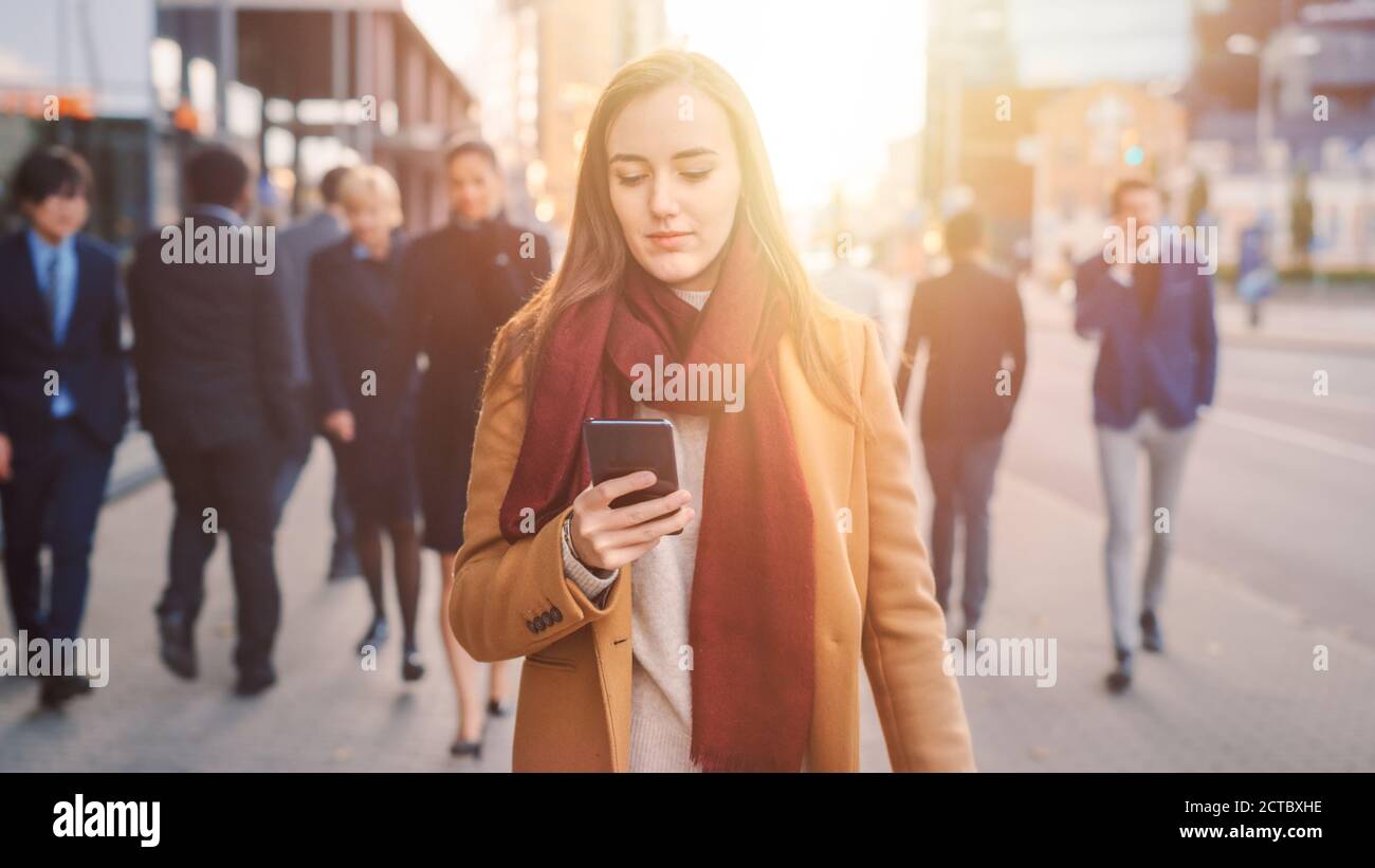 Junge lässig gekleidete Frau ist mit einem Smartphone auf einer Straße. Geschäftsleute und Büroleiter gehen Pass auf ihrem Weg zur Arbeit. Sie Sieht Aus Stockfoto