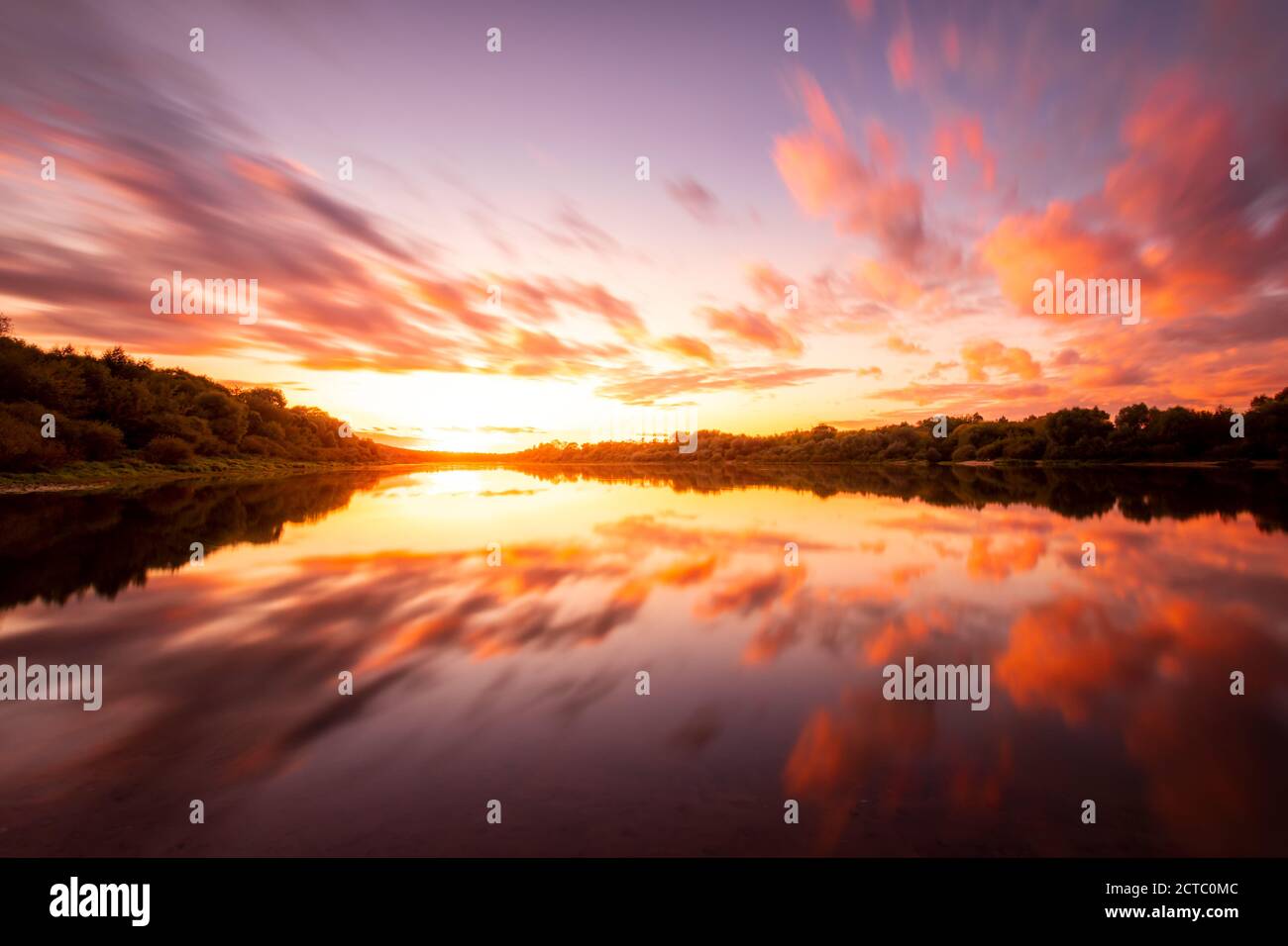 Eine Sonnenuntergangs- oder Sonnenaufgangsszene über einem See oder Fluss mit dramatisch bewölktem Himmel, der sich an einem Sommerabend oder Morgen im Wasser spiegelt. Stockfoto