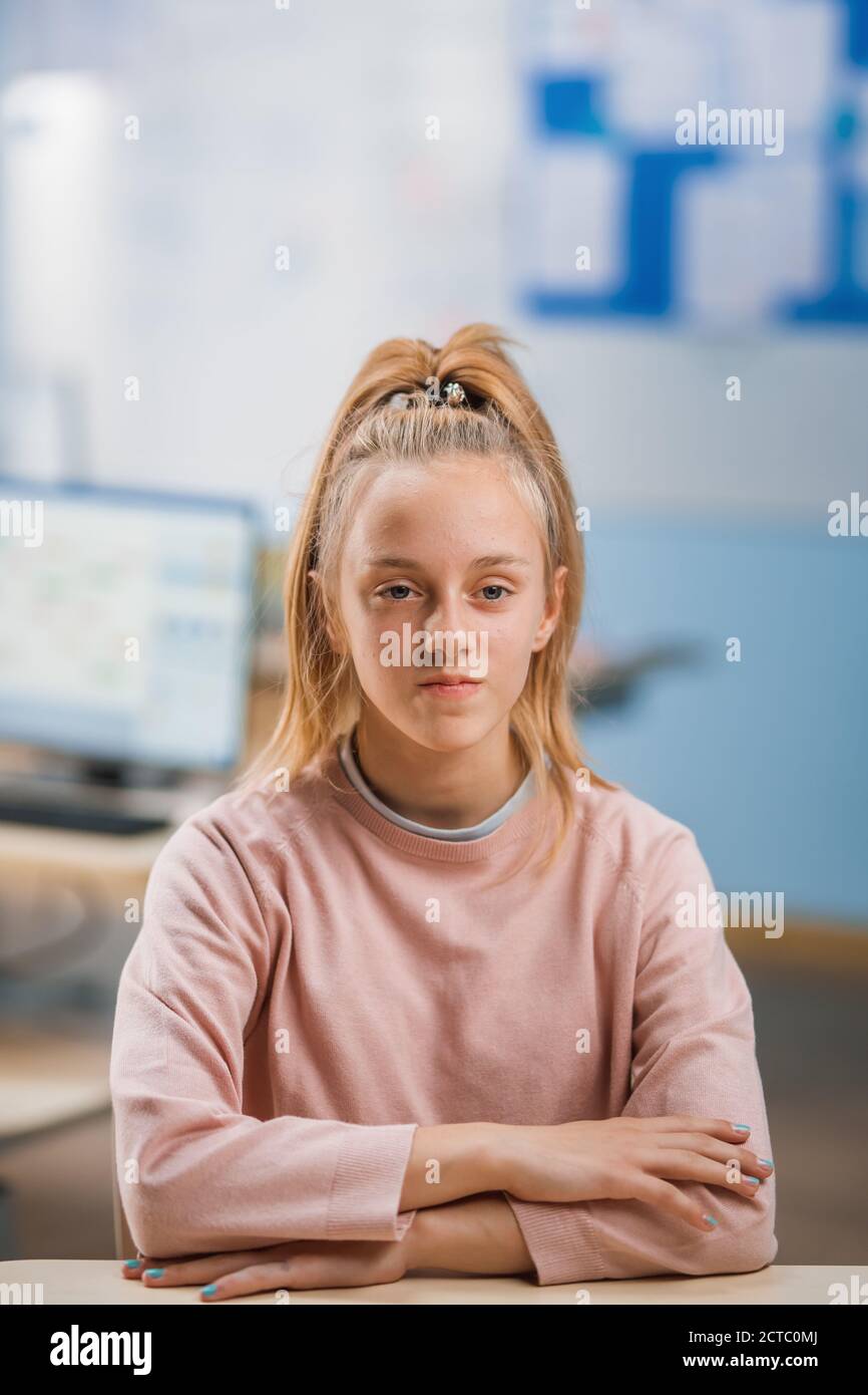 Grundschule Klassenzimmer: Portrait eines niedlichen kleinen Mädchen mit blondem Haar und Pferdeschwanz folgt Klassenregeln und sitzt richtig. Brilliant Young Stockfoto