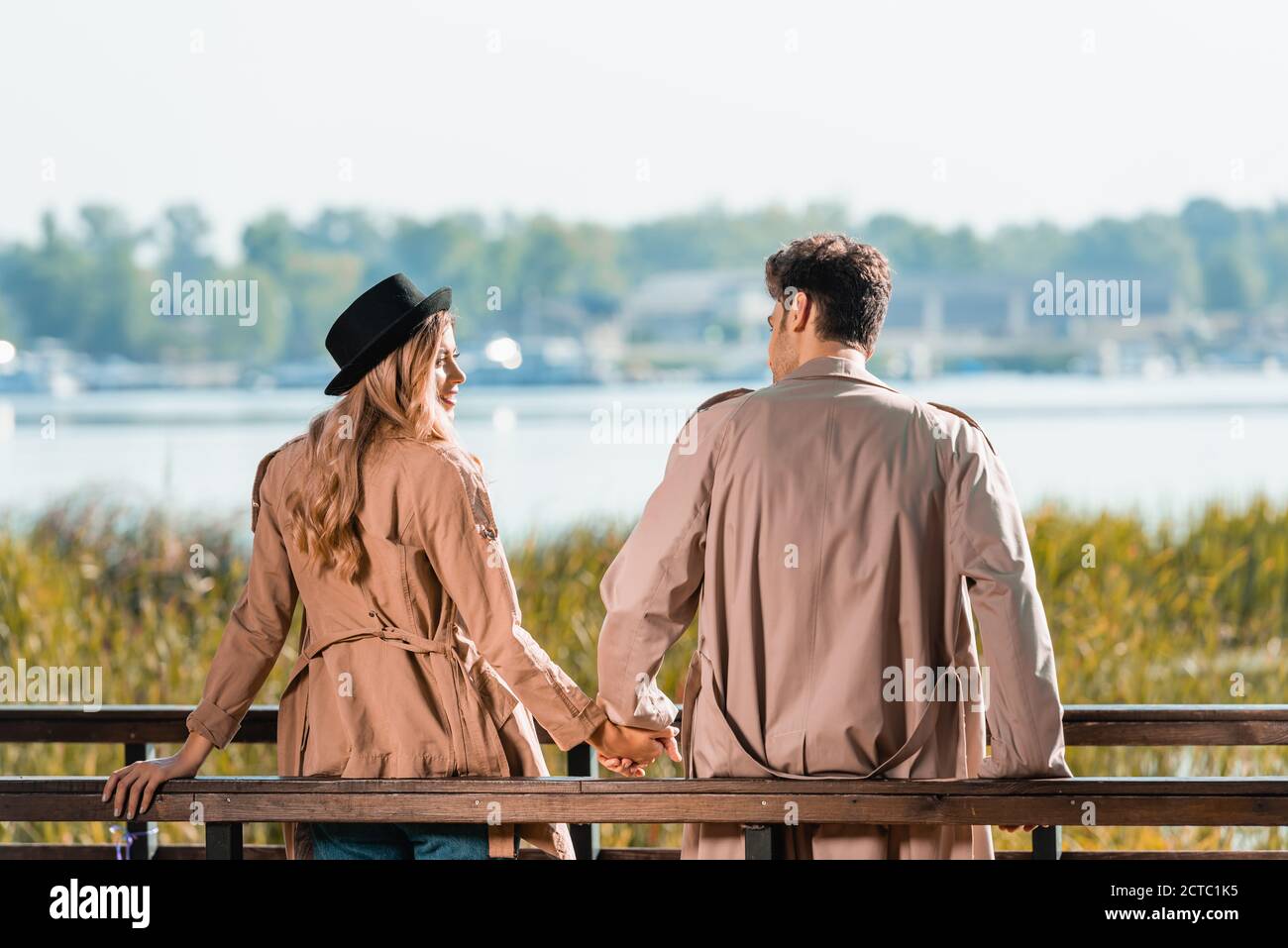 Paar in Trenchcoats Blick auf einander und halten Hände Stockfoto