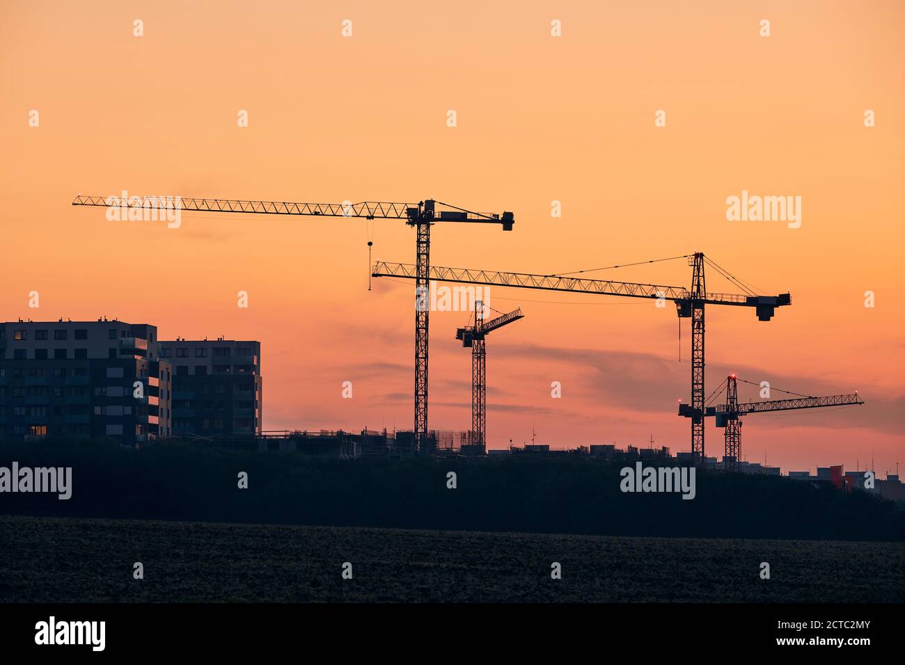 Bauaktivitäten auf Baustellen. Silhouetten von Kranichen gegen den goldenen Himmel. Stockfoto