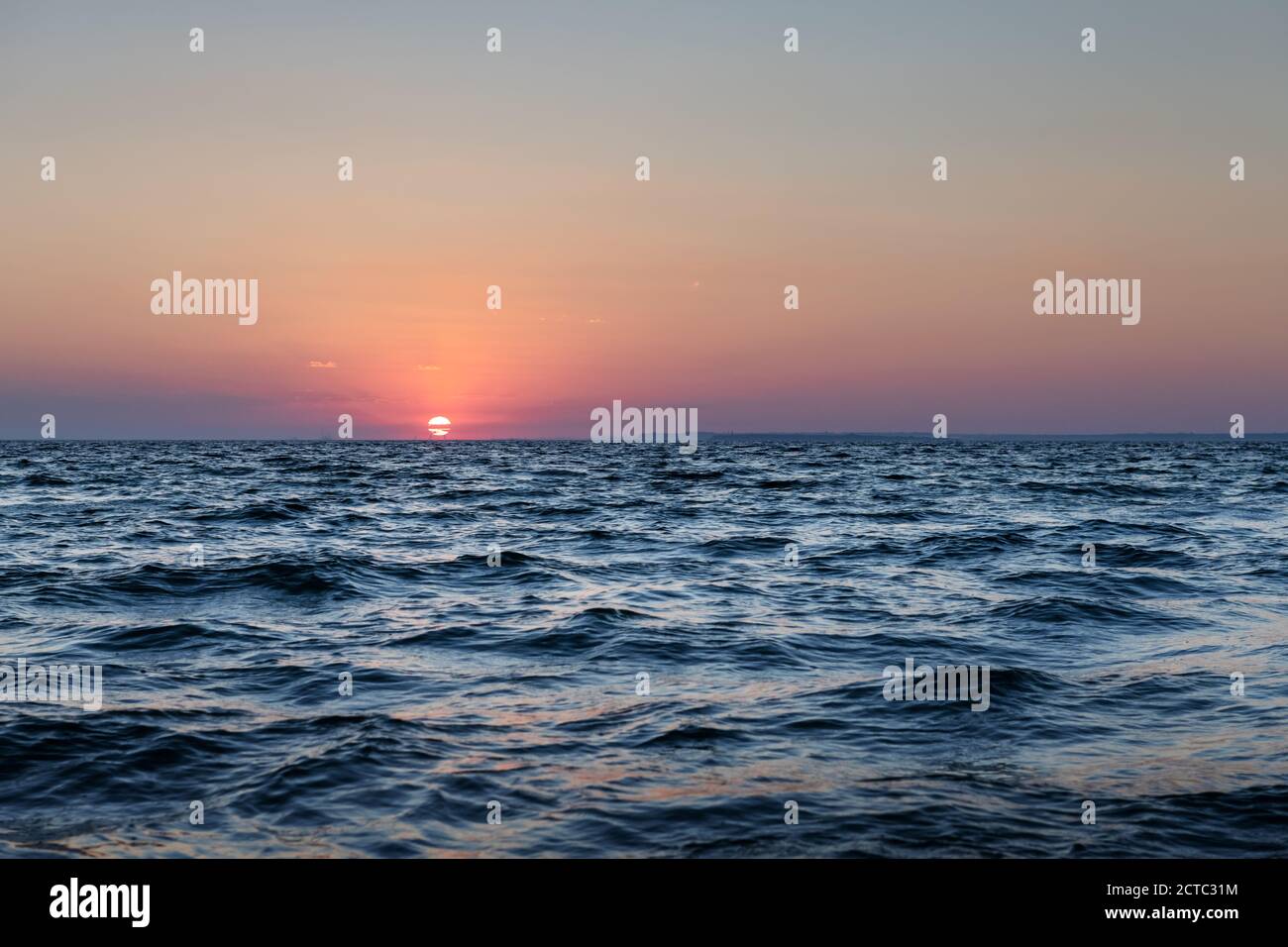 Sonnenuntergang im Meer mit großer Sonnendämmerung sanfte Wellen und rot bewölkter Himmel. Hintergrund des Sonnenaufgangs. Landschaftsfotografie Stockfoto