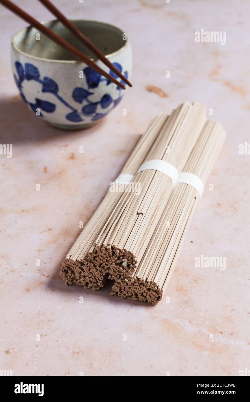 Drei Bündel trockener japanischer Soba-Nudeln mit einer leeren Nudel-Keramikschale und hölzernen Essstäbchen. Stockfoto