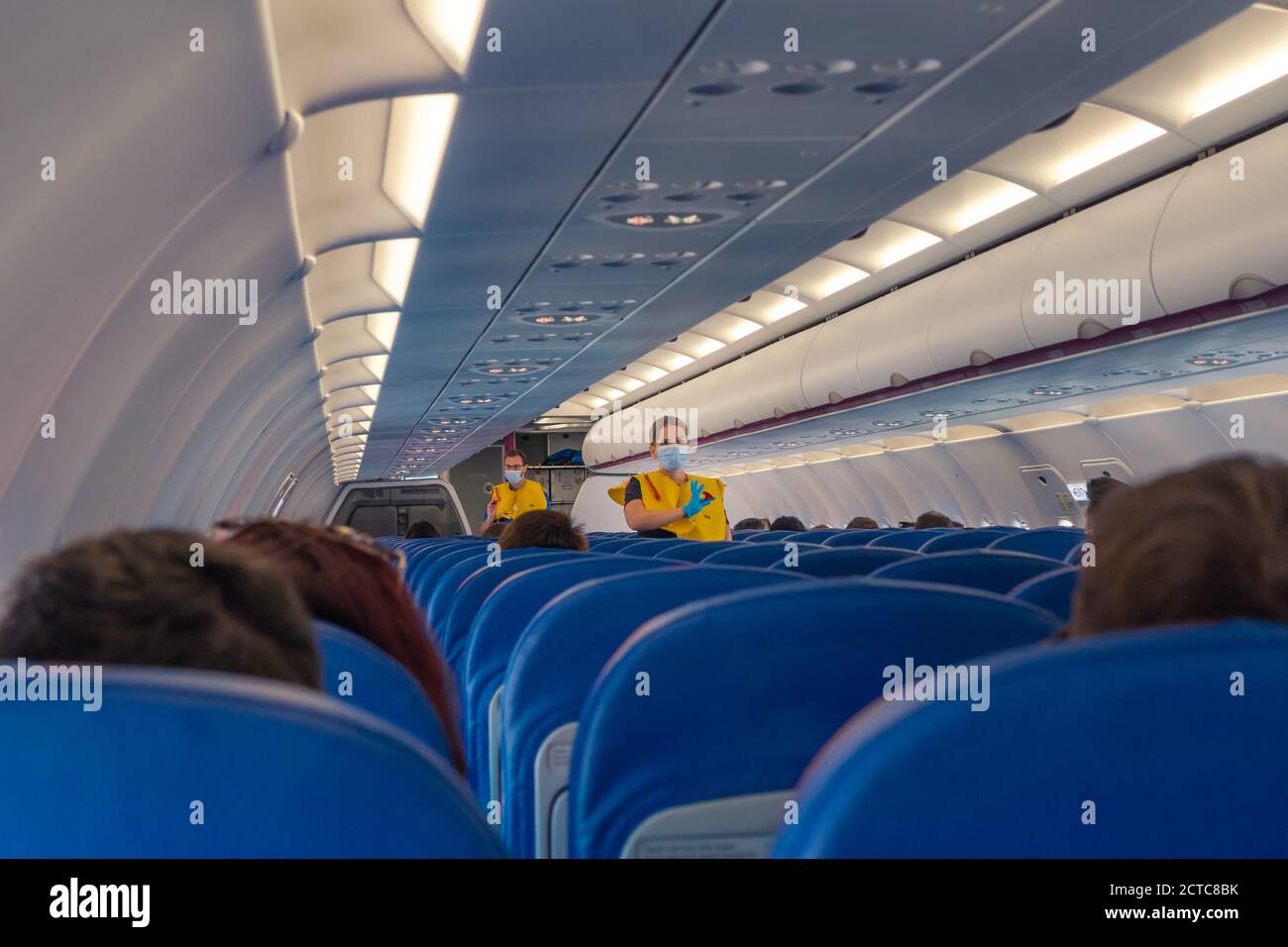 Stewardess in OP-Maske und gelb Westen geben Anweisungen an die Passagiere. Halb leeres Flugzeug aufgrund einer COVID-Pandemie. Stockfoto