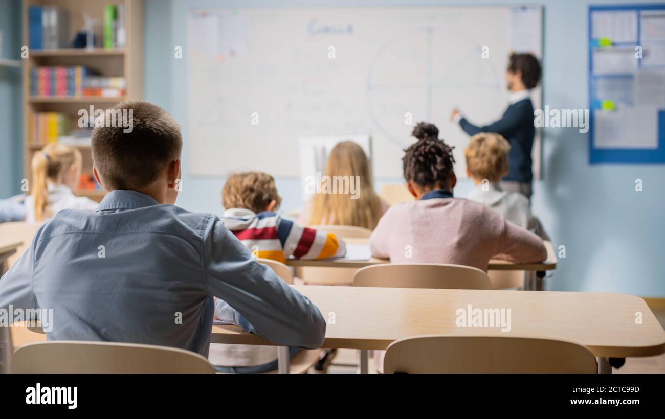 Talentierter Lehrer erklärt Lektion zu einem Klassenzimmer voller heller vielfältiger Kinder. In der Grundschule mit Gruppe von Smart Kids Learning Science und Stockfoto