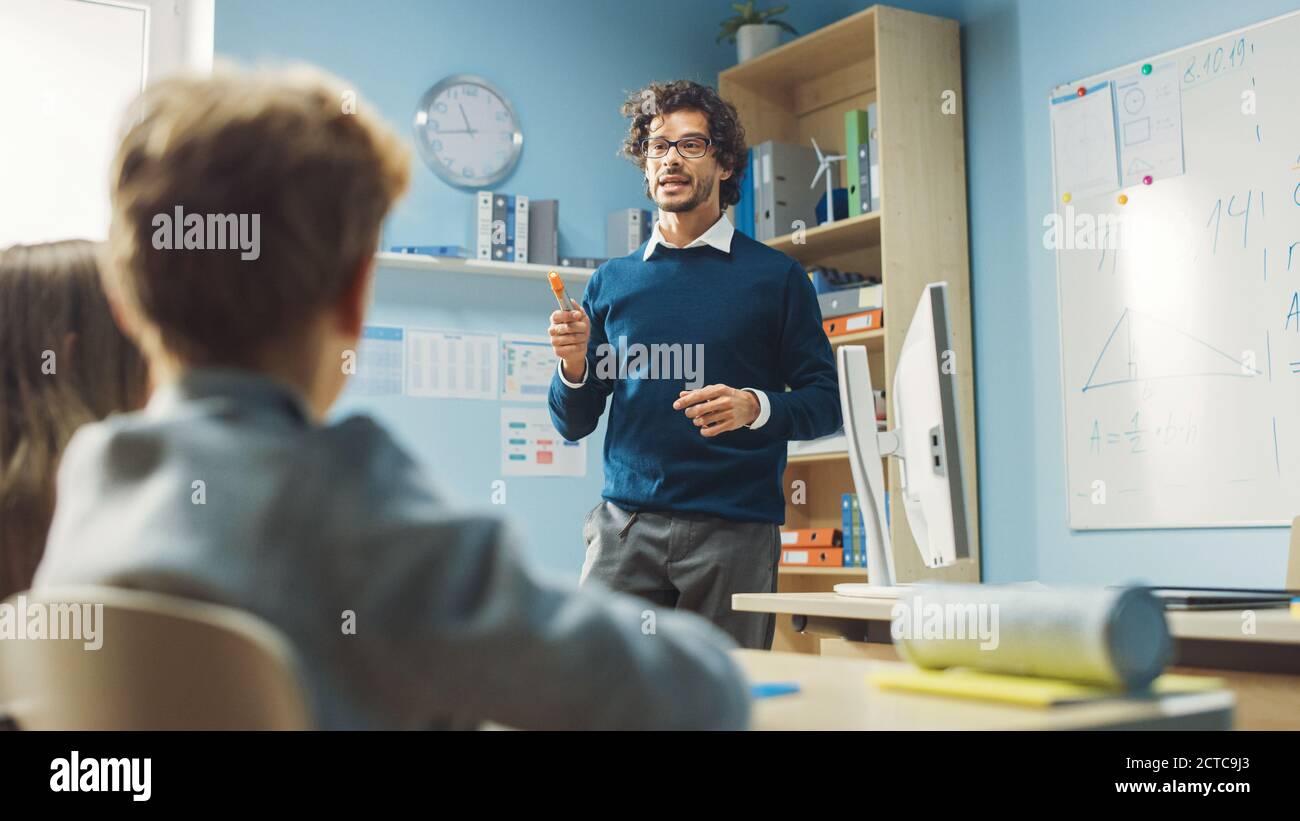 Enthusiastischer Lehrer erklärt Lektion zu einem Klassenzimmer voller heller vielfältiger Kinder, führt Lektion mit Fragen stellen. In Grundschule Gruppe von Stockfoto