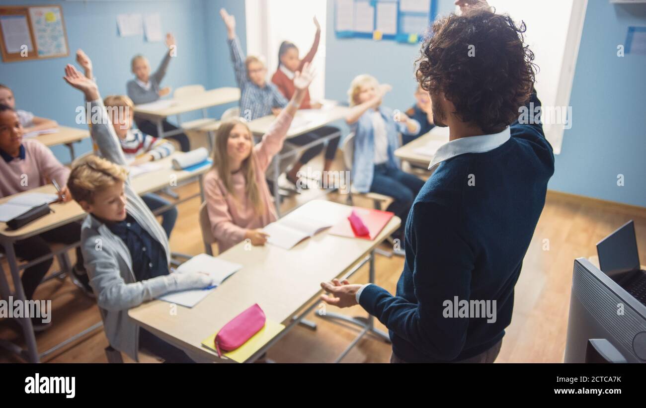 Elementare Klassenzimmer von verschiedenen hellen Kindern Hören auf den Lehrer eine Lektion geben. Jeder hebt die Hand und weiß, welche Antwort richtig ist. Brillant Stockfoto