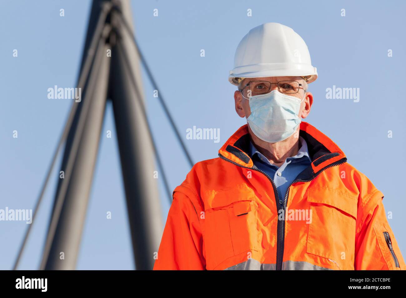 Architekt oder Ingenieur mit Gesichtsmaske und Schutzkleidung Vor einem industriellen Hintergrund - konzentrieren Sie sich auf die Gesicht Stockfoto