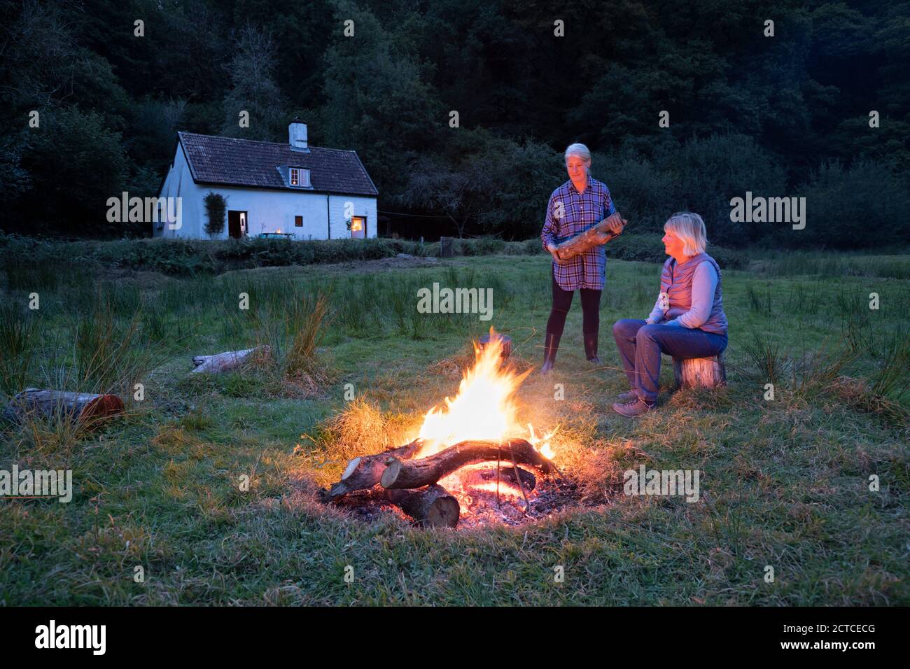 Zwei Frauen versammelten sich um Lagerfeuer mit Landhaus im Hintergrund im Herbst, Exmoor, Somerset, England, Großbritannien, Europa Stockfoto