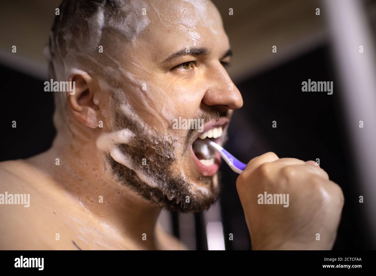 Brunette Mann Bürsten seine Zähne seifen seinen Kopf und Bart Mit Haarpflegeprodukt Stockfoto
