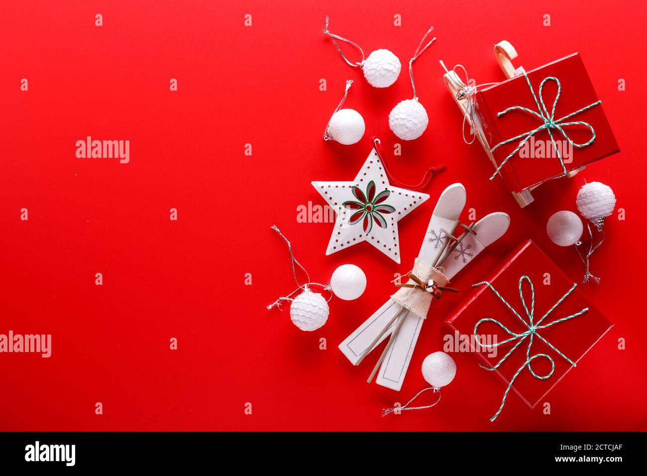Draufsicht auf rotem Hintergrund mit roten Geschenkschachteln, Sternornamenten und kleinen Holzskiern und Schlitten für die Weihnachtsferien Stockfoto