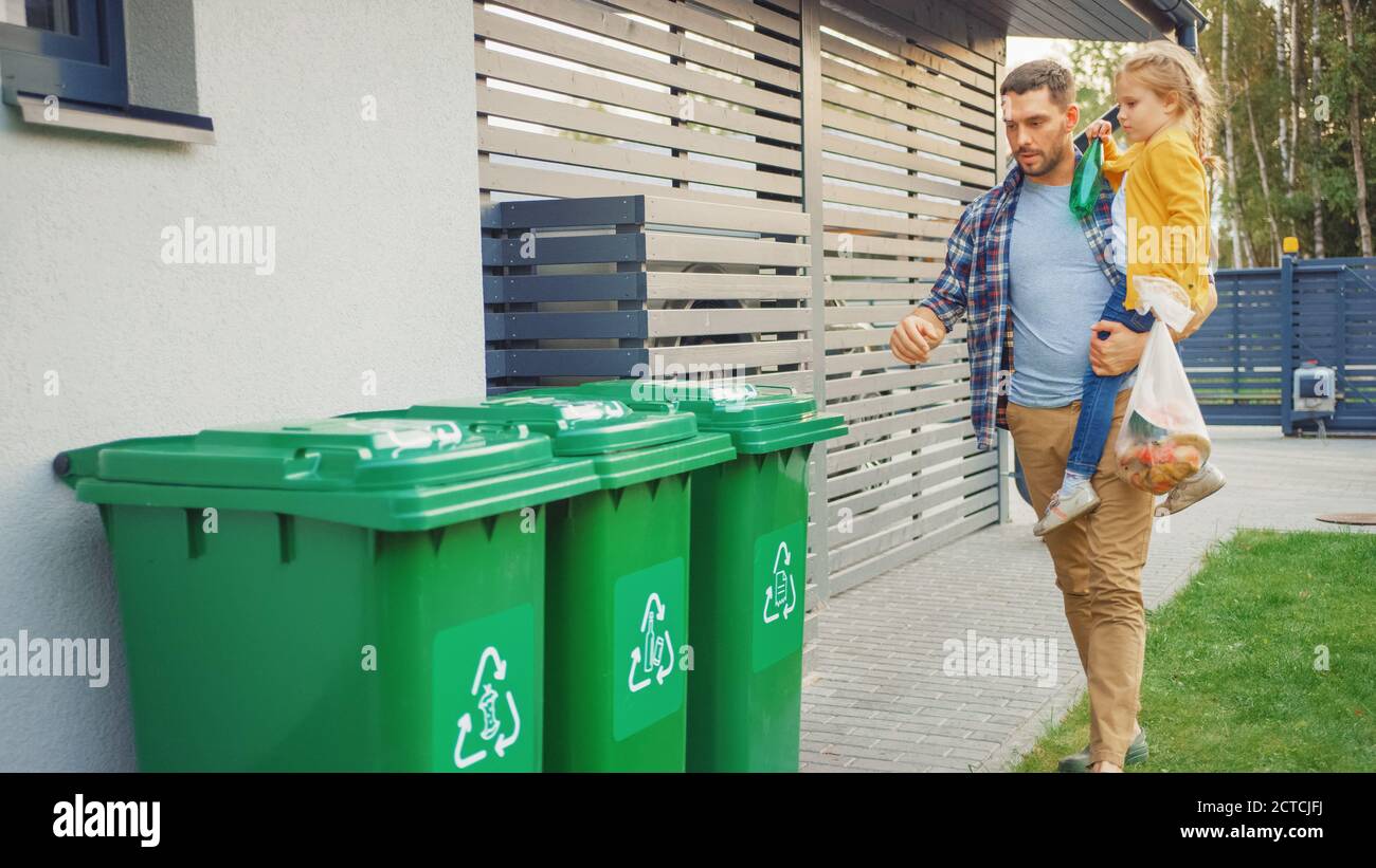 Vater hält ein junges Mädchen und wird eine leere Flasche und Lebensmittelabfälle in den Müll werfen. Sie Verwenden Richtige Mülltonnen, Weil Diese Familie Stockfoto