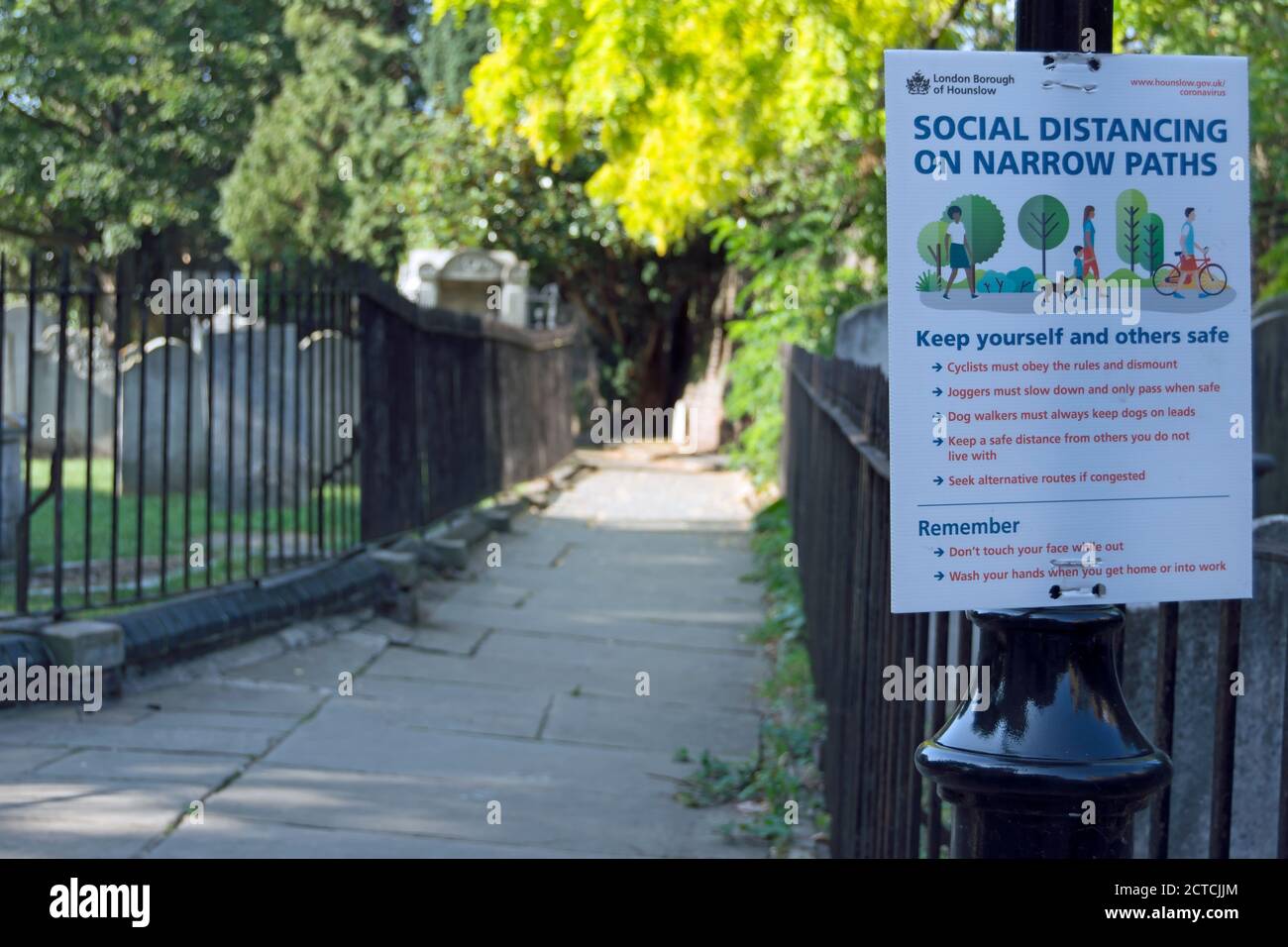 Hinweis beschreibt Regeln für soziale Distanzierung auf schmalen Wegen, neben einem schmalen Pfad im Hof der St. nicholas' Church, chiswick, london, england Stockfoto