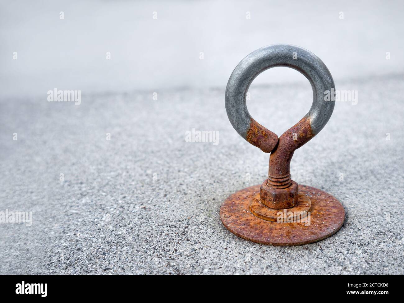 Rostige Öse oder Ösenschraube. Nahaufnahme. Mit einer Zementfliese im Freien verschraubt, die den Abfluss auf der Terrasse abdeckt. Ösen werden zur Befestigung von Seilen oder Kabeln verwendet. Stockfoto