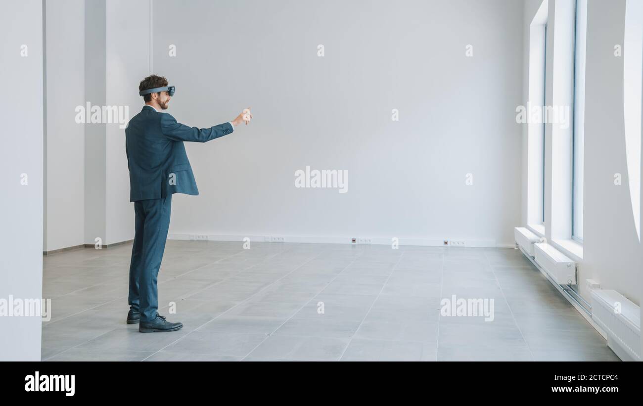 Geschäftsmann in Holographic Augmented Reality Brille steht im leeren Büro und Karte. Sonnenlicht Scheint Durch Große Fenster. Stockfoto