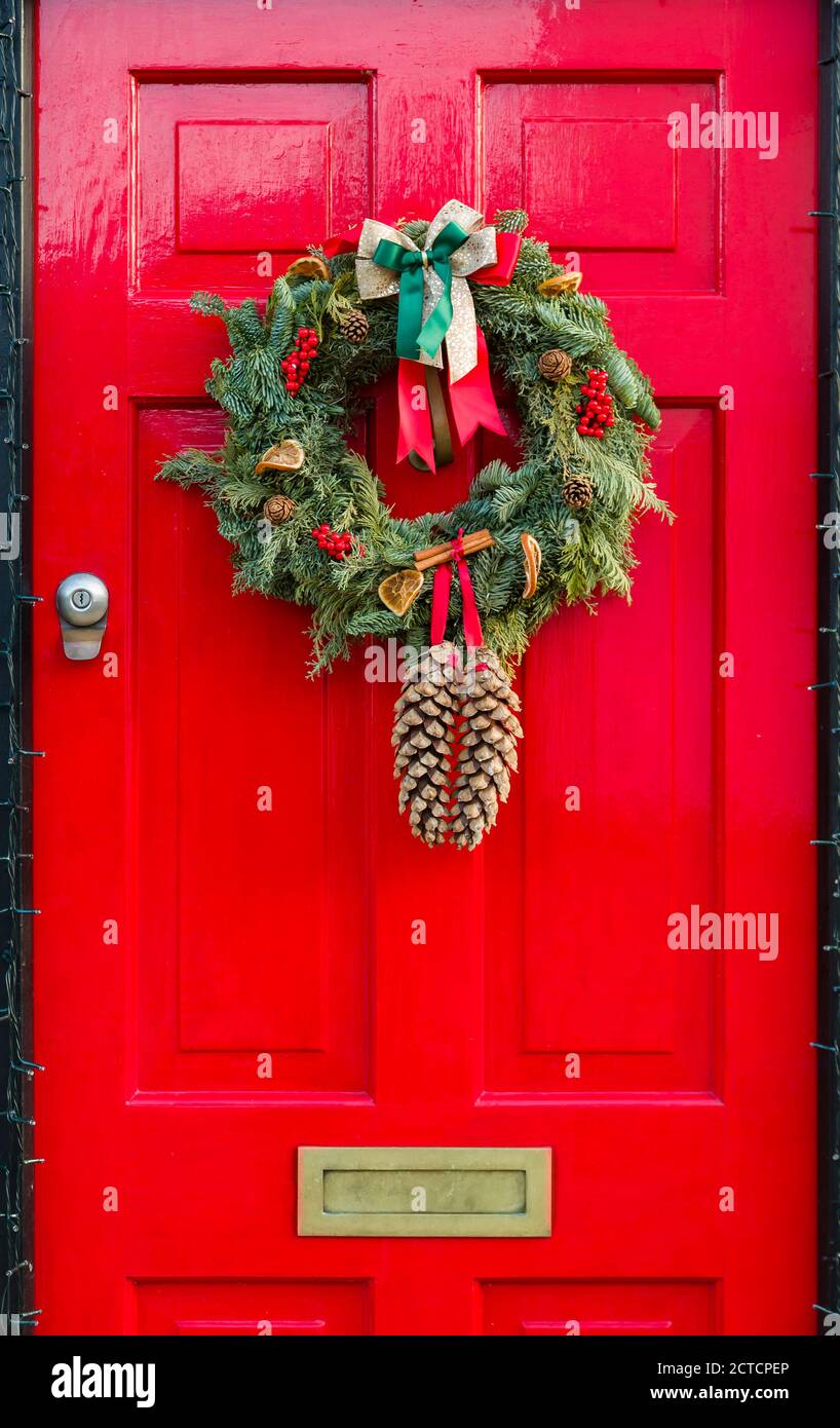 Detail der hölzernen Vordertür zu einem britischen Haus gemalt Ein festliches leuchtendes Rot mit Weihnachtskranz Stockfoto