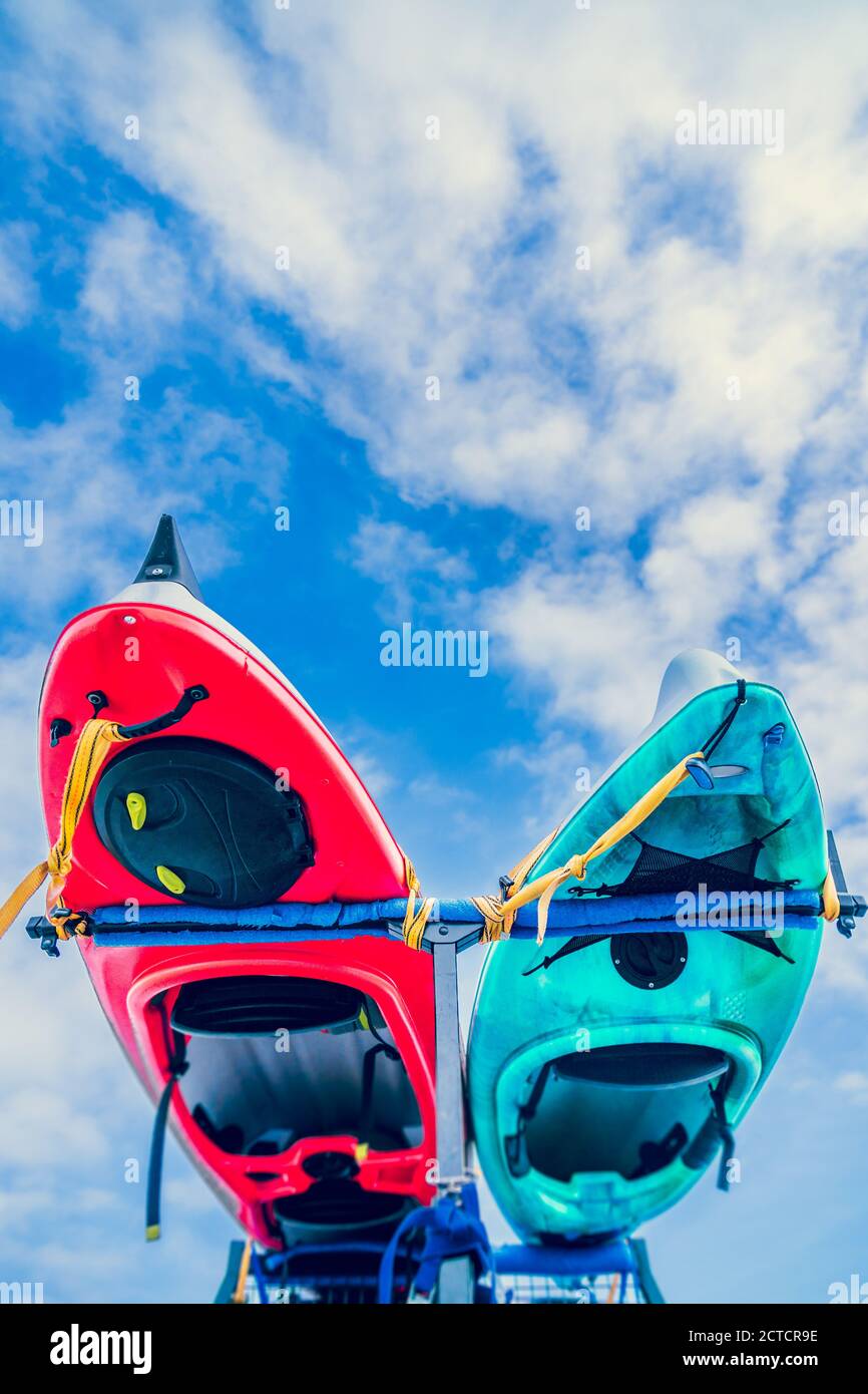Darunter ein paar bunte Seekajaks, die an den Transport gebunden sind Rack gegen einen blauen Himmel mit Wolken und Copyspace Stockfoto