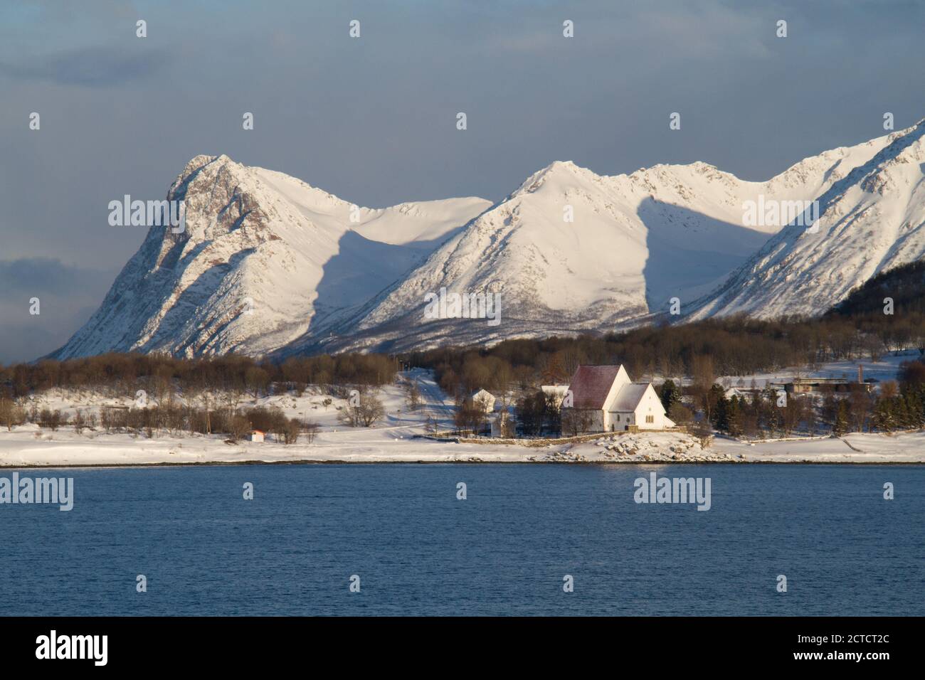 Verschneite Berggipfel bilden die Kulisse für die kleine Trondenes Kirche in Harstad, Norwegen Stockfoto