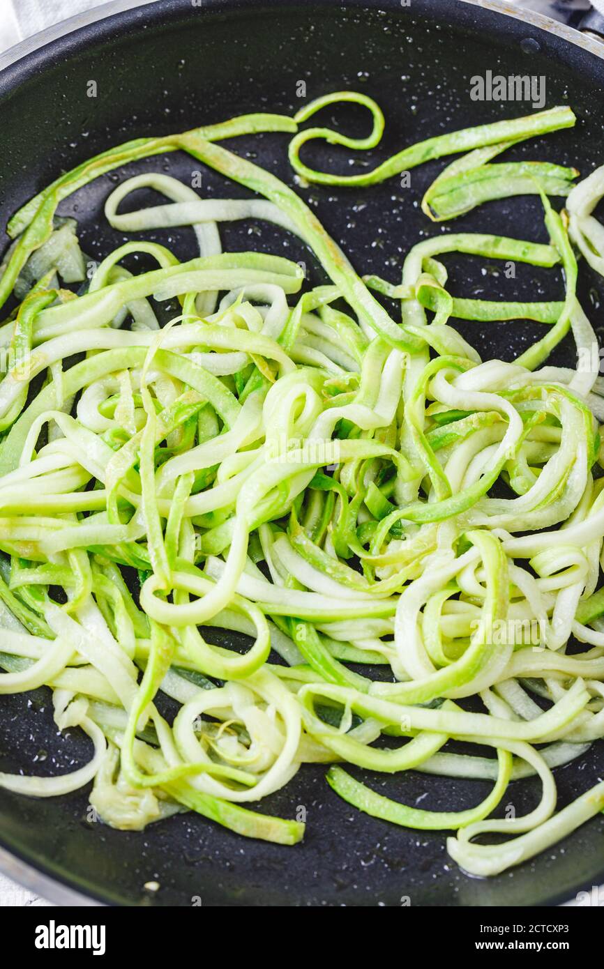 Zucchini-Nudeln in Bratpfanne auf weißem Hintergrund. Vegetarisches Gericht. Stockfoto