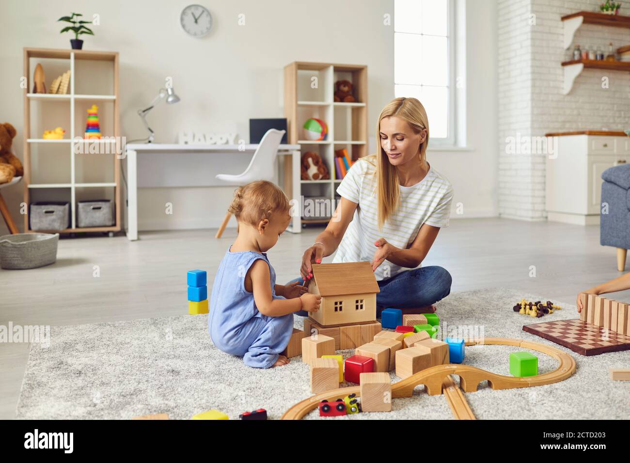 Junge Mutter spielt mit niedlichen kleinen Sohn und lehrt ihn Spielzeughaus in gemütlicher moderner Wohnung zu bauen Stockfoto