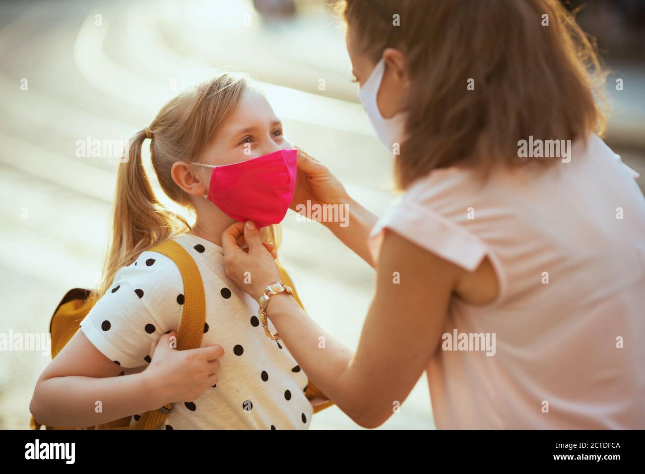 Leben während Coronavirus Pandemie. Elegante Mutter und Schulmädchen mit Masken und gelben Rucksack immer bereit für die Schule im Freien. Stockfoto