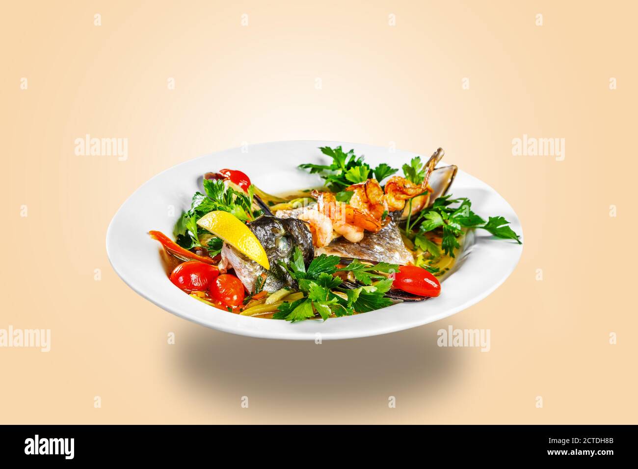 Der Kopf der Fische, Muscheln, Gemüse und Garnelen sind auf einem weißen Teller. Restaurant-Service. Die Platte schwimmt in der Luft Stockfoto