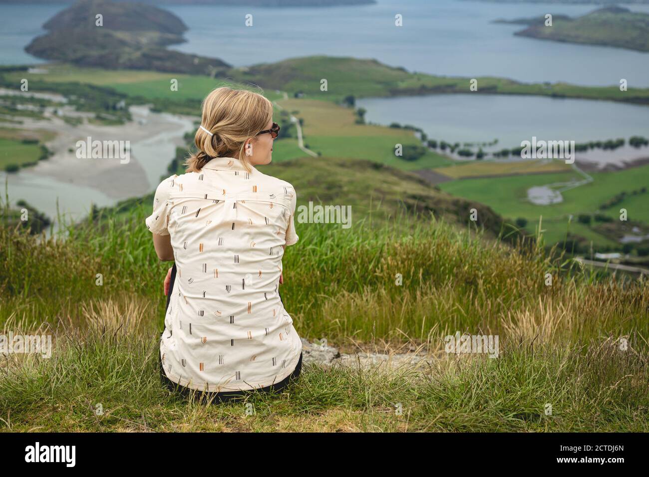 Junge Frau, die auf dem Rocky Mountain sitzt und auf den Lake Wanaka, Neuseeland blickt Stockfoto