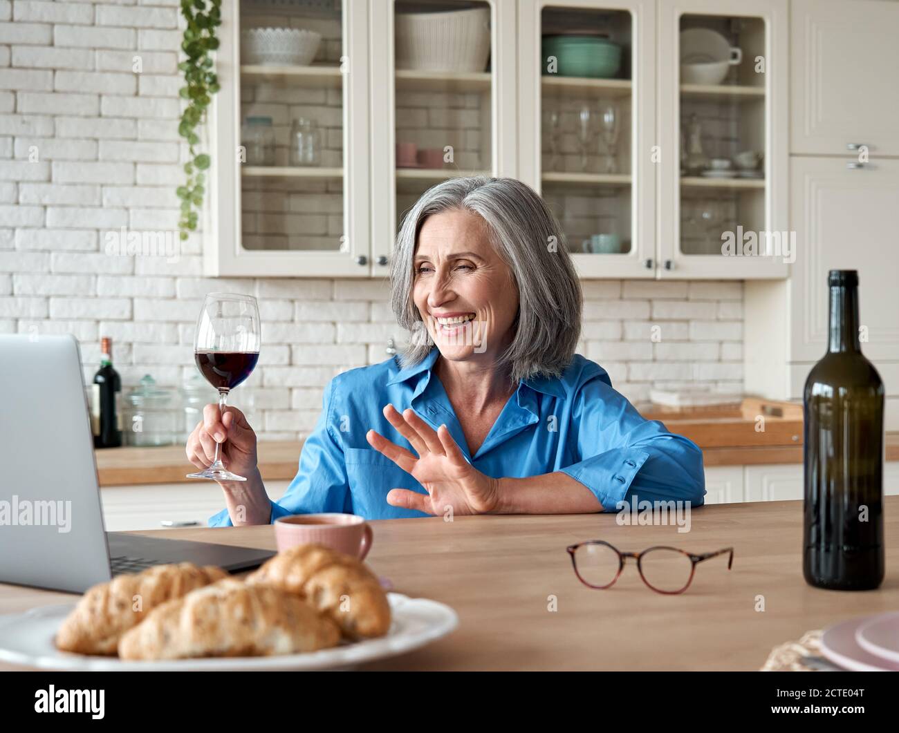 Glücklich 60s reife Frau trinken Wein Video Anruf Freund auf Laptop zu Hause. Stockfoto