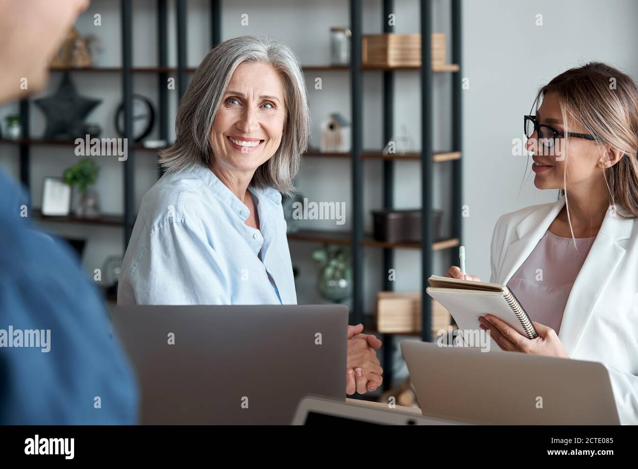 Lächelnd reife weibliche Mentorin Lehrerin, die mit Studenten oder Praktikanten kommuniziert. Stockfoto