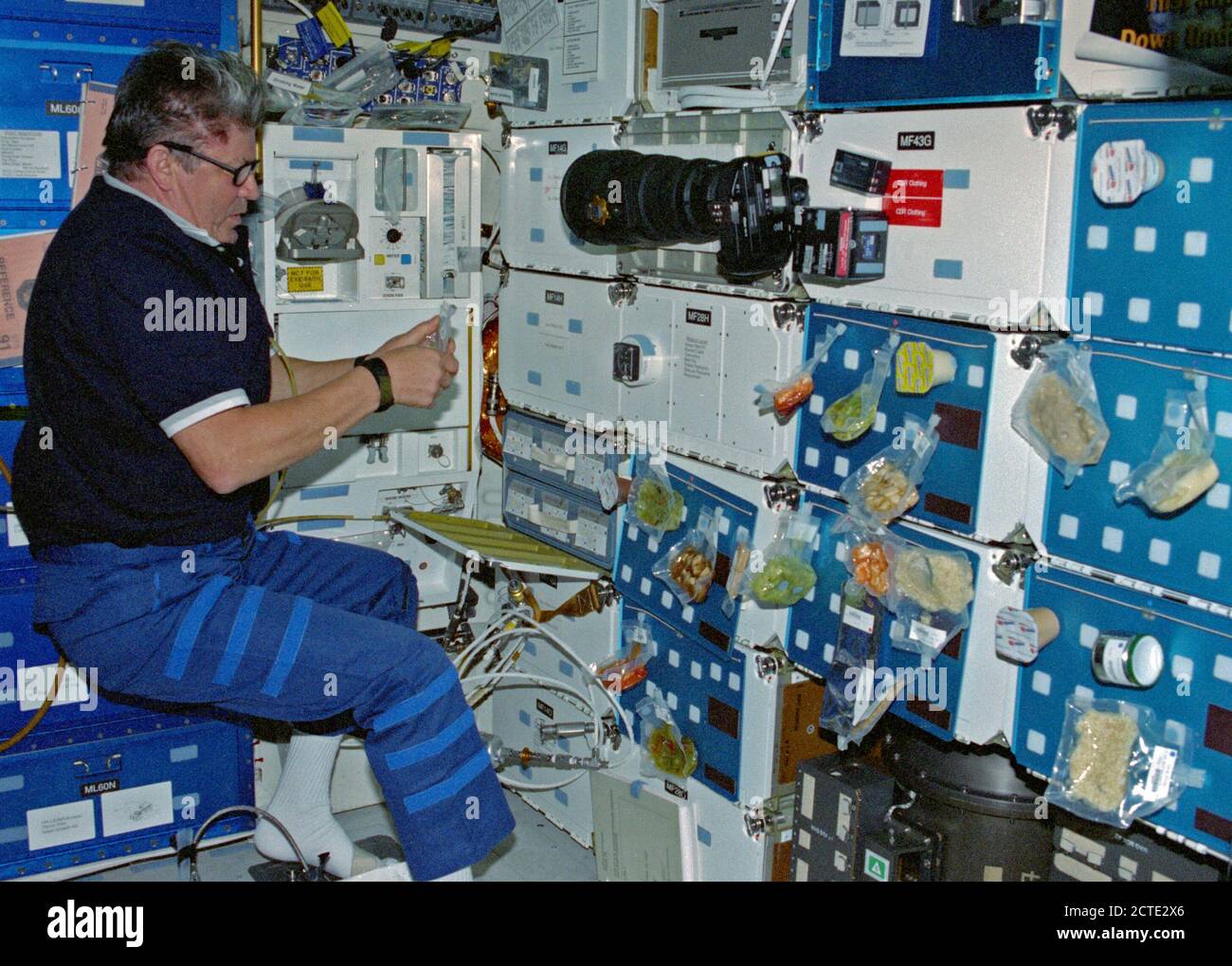 (12 Juni 1998) - - - Kosmonaut Valery V. Ryumin, Vertreter der russischen Raumfahrtagentur (RSA), organisiert eine Mahlzeit auf dem Deck der Erdumlaufbahn Space Shuttle Discovery. Die Pantry ist an der Ecke der mittleren Deck Schließfächer befinden. Stockfoto