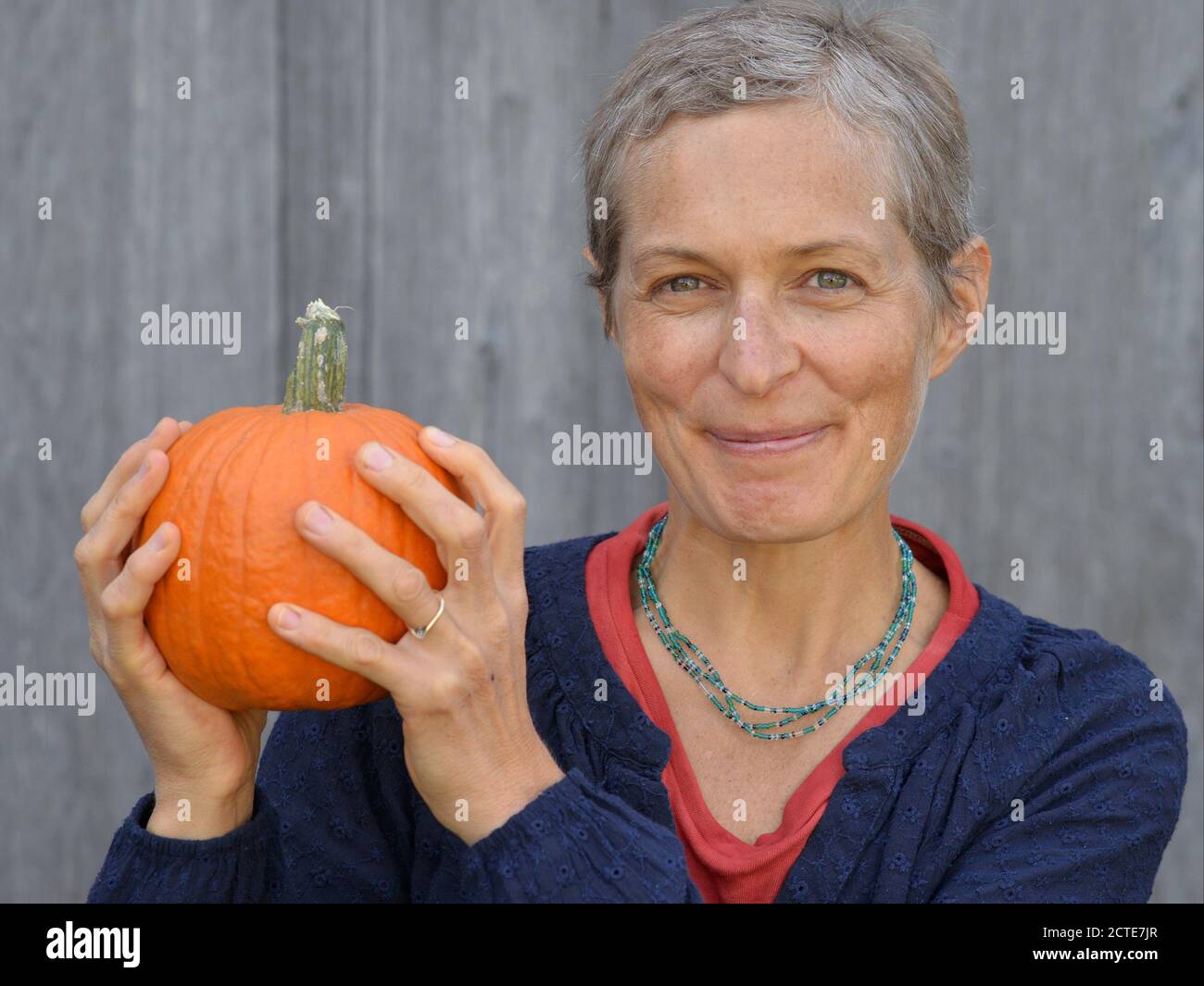 Die kaukasische kanadische Landsfrau mittleren Alters mit kurzen Haaren hält einen Kürbis in den Händen und schaut auf die Kamera. Stockfoto