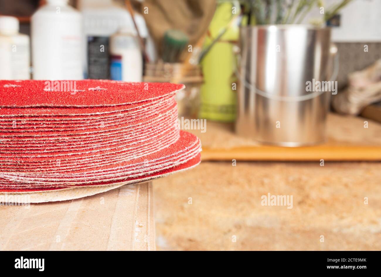 Mehrere Schleifpads für Schleifer oder Bohrer auf Werkstatttisch. Konzentrieren Sie sich auf den Stapel von roten Schleifscheiben, weichen verschwommenen Hintergrund Sägemehl Tisch, Flasche Stockfoto