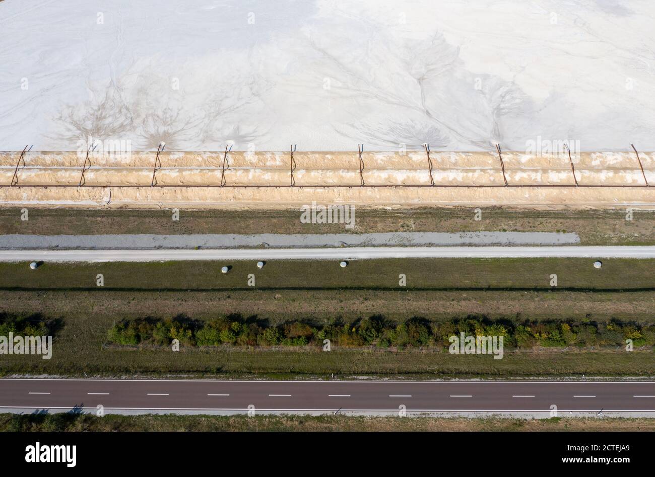 17. September 2020, Sachsen-Anhalt, Latdorf: Eine Landstraße führt entlang des Staudamms eines Lindenteiches. Die mehrere Hektar großen Absetzbecken werden zur Aufbereitung von Produktionsabwässern aus der Sodaproduktion eingesetzt. Dabei setzen sich Kalk und Rückstände ab, das gereinigte Wasser fließt in die Saale. Die Sedimente bewirken, dass die Hügel stetig wachsen. Die Solvay GmbH produziert seit 130 Jahren Soda, Natriumhydrogencarbonat, hochreines Wasserstoffperoxid und hochreine Phosphorsäure für die Herstellung von Computerchips. (Luftaufnahme mit Drohne) Foto: Jan Woitas/dpa-Zentralbild/ZB Stockfoto